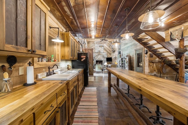 kitchen with sink, wood walls, wood ceiling, black refrigerator, and pendant lighting