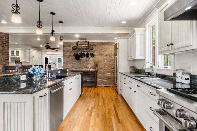 kitchen with extractor fan, sink, hanging light fixtures, brick wall, and white cabinets