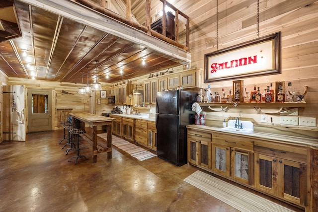 kitchen featuring sink, black fridge, wood ceiling, concrete floors, and wooden walls