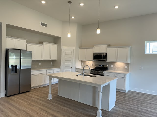 kitchen featuring sink, hardwood / wood-style floors, pendant lighting, white cabinets, and appliances with stainless steel finishes