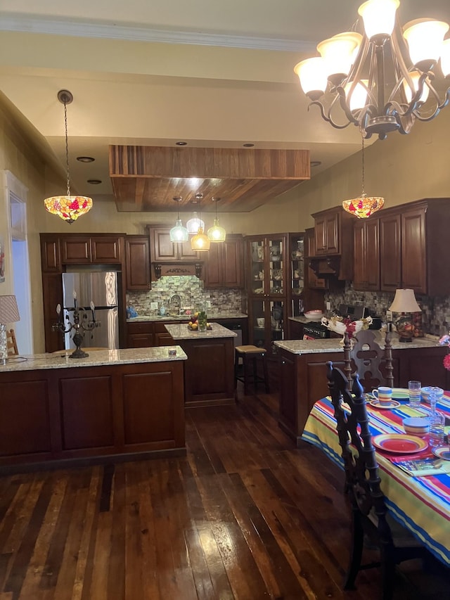 kitchen featuring pendant lighting, stainless steel fridge, tasteful backsplash, light stone counters, and a chandelier