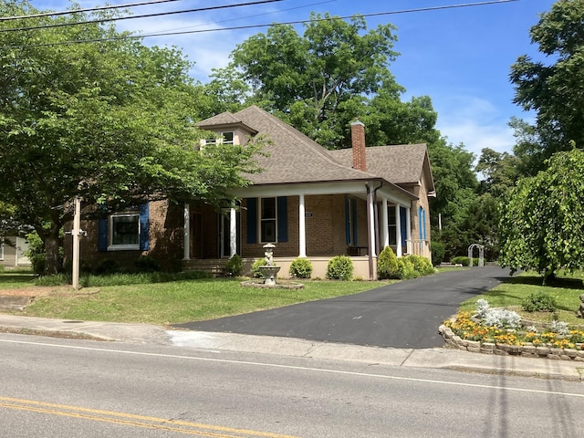 view of front facade featuring driveway, brick siding, a shingled roof, a chimney, and a front yard