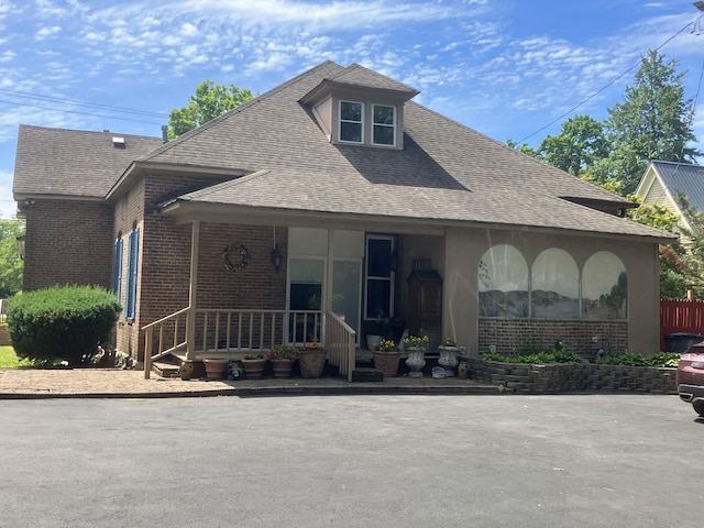 view of front facade with covered porch, brick siding, and roof with shingles