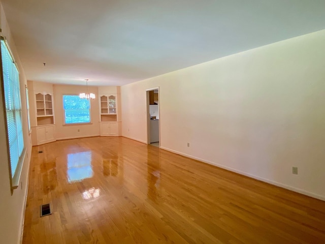 empty room featuring built in shelves, a chandelier, and hardwood / wood-style floors