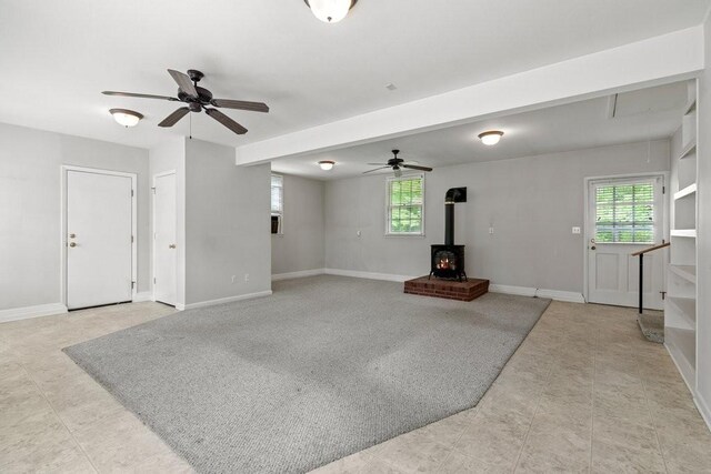 living room featuring a healthy amount of sunlight, a wood stove, and ceiling fan