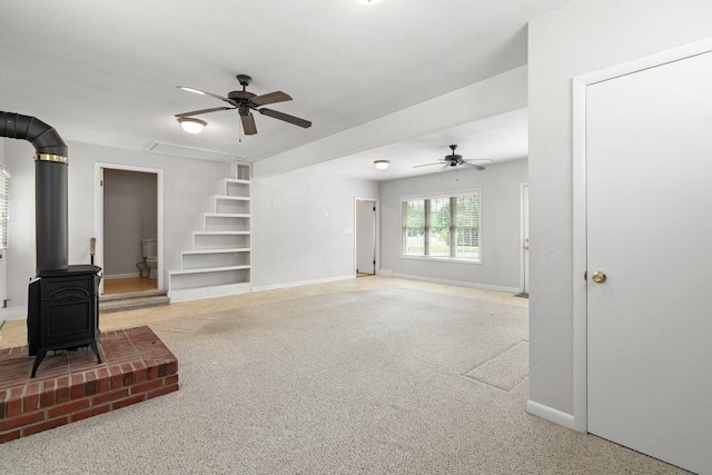 living room featuring a wood stove, light colored carpet, built in features, and ceiling fan