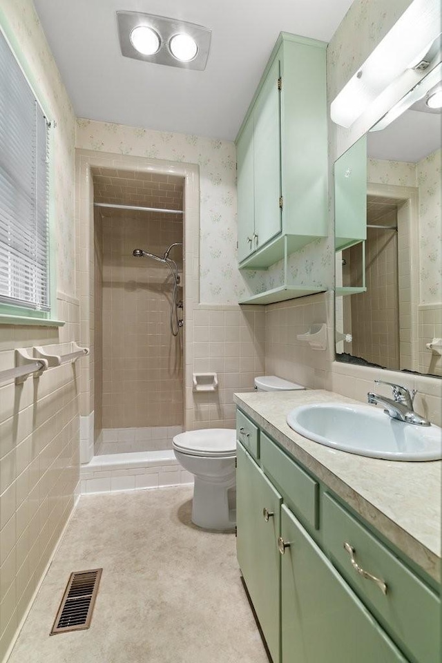 bathroom featuring a tile shower, tile walls, vanity, toilet, and tile patterned floors