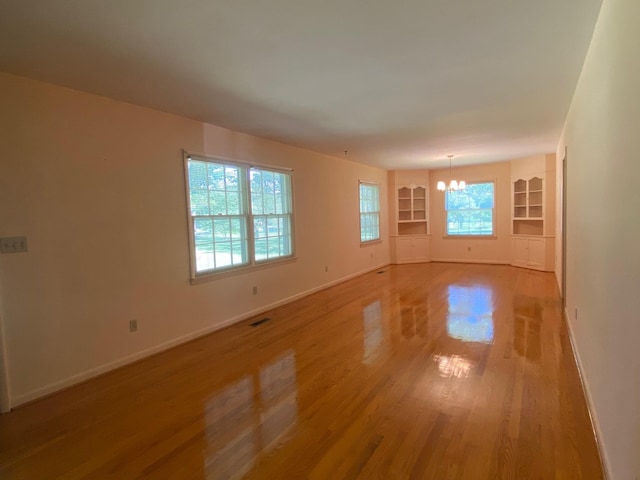 empty room with light wood-type flooring, built in features, and an inviting chandelier