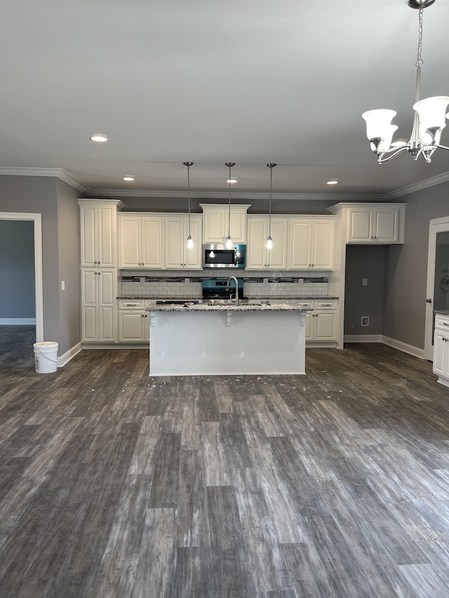 kitchen with an island with sink, ornamental molding, light stone counters, and decorative light fixtures