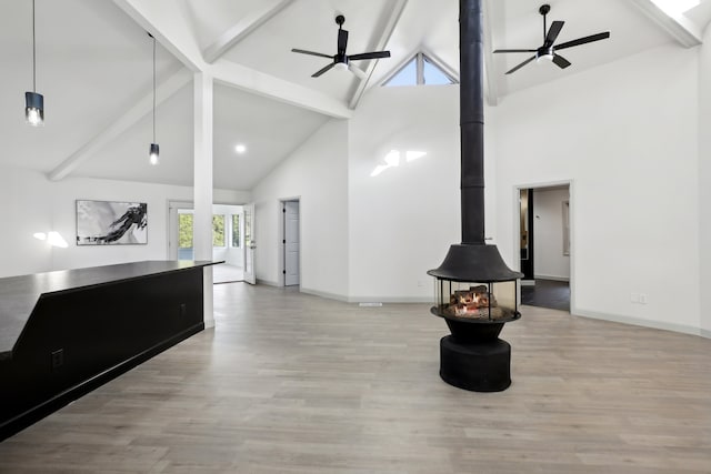 interior space with a wood stove, wood finished floors, a ceiling fan, and beamed ceiling