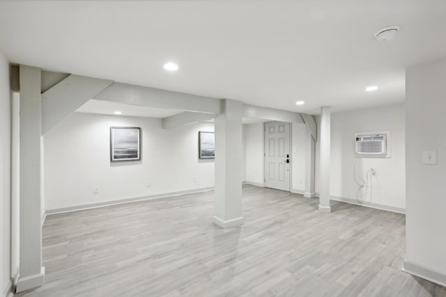 finished below grade area with baseboards, a wall mounted air conditioner, light wood-style flooring, and recessed lighting