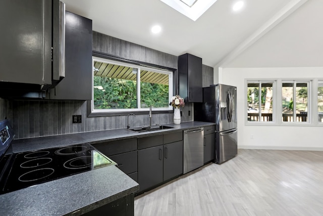 kitchen featuring stainless steel appliances, dark countertops, tasteful backsplash, lofted ceiling with skylight, and a sink