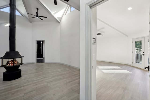 living room with baseboards, a ceiling fan, wood finished floors, a wood stove, and high vaulted ceiling