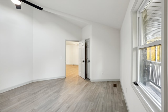 unfurnished room featuring lofted ceiling, light wood finished floors, baseboards, and a wealth of natural light