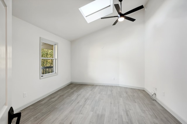 empty room featuring ceiling fan, vaulted ceiling with skylight, light wood-style flooring, and baseboards