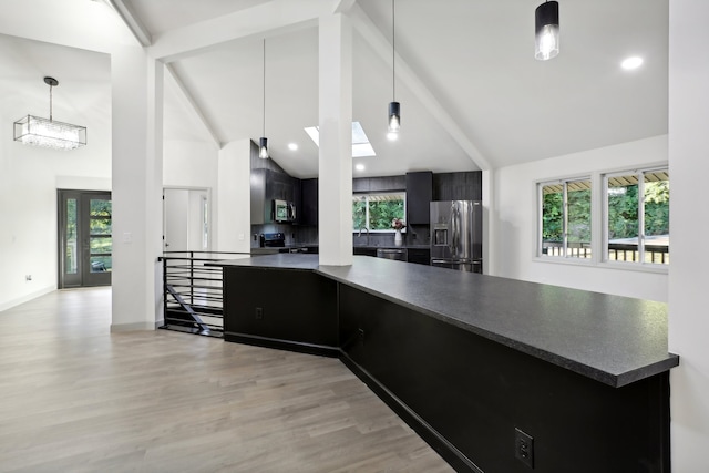 kitchen featuring dark countertops, appliances with stainless steel finishes, dark cabinets, light wood-type flooring, and beam ceiling