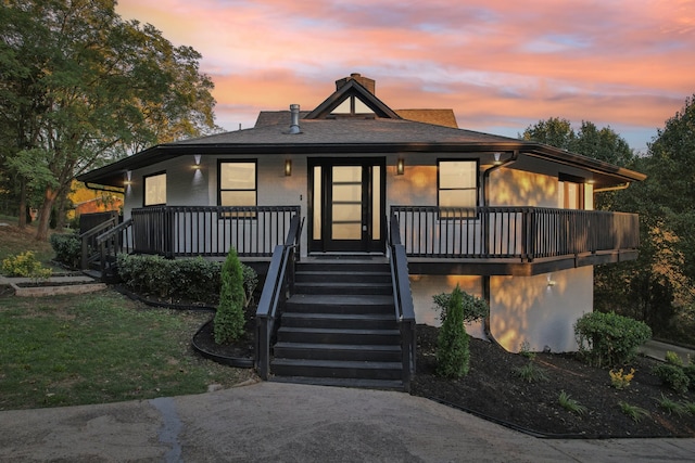 view of front of property with a shingled roof, a chimney, covered porch, stairs, and a yard