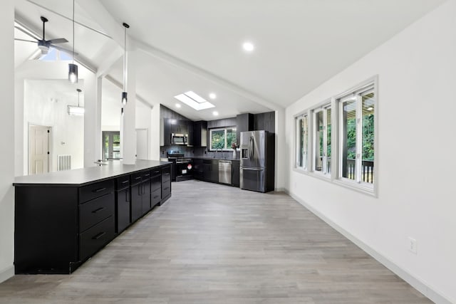 kitchen featuring dark cabinets, stainless steel appliances, baseboards, light wood-style floors, and lofted ceiling with skylight