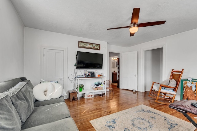 living room featuring dark wood-type flooring, a textured ceiling, and ceiling fan