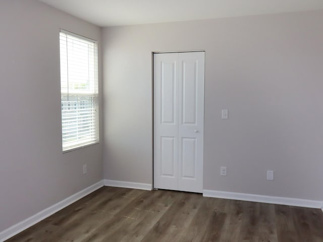 unfurnished bedroom featuring dark hardwood / wood-style flooring, a closet, and multiple windows