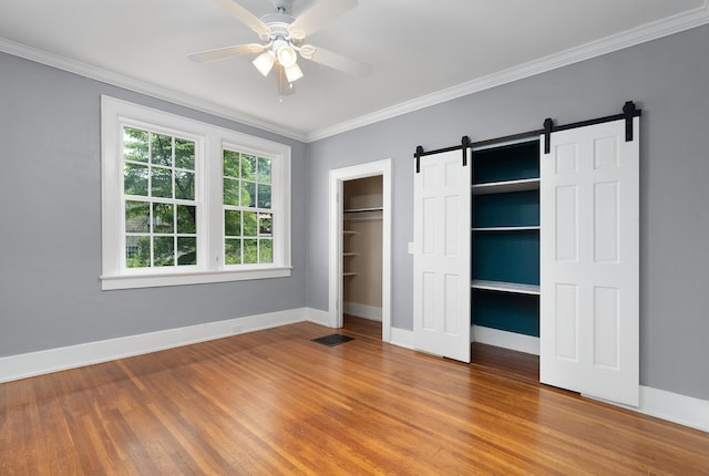 unfurnished bedroom featuring a barn door, ceiling fan, ornamental molding, and hardwood / wood-style flooring