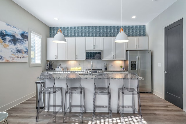 kitchen with an island with sink, decorative light fixtures, dark wood-type flooring, and stainless steel appliances