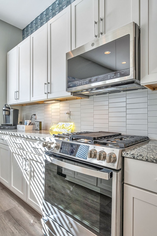 kitchen with light stone countertops, appliances with stainless steel finishes, white cabinets, hardwood / wood-style flooring, and backsplash