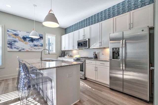 kitchen with light hardwood / wood-style floors, stainless steel appliances, backsplash, a kitchen island with sink, and white cabinets