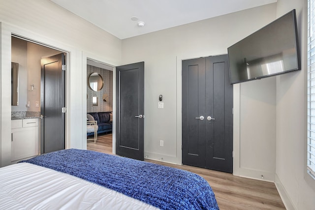 bedroom with connected bathroom and light hardwood / wood-style flooring