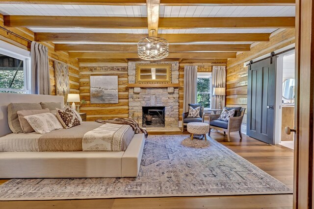 bedroom featuring wooden walls, hardwood / wood-style floors, beam ceiling, a stone fireplace, and a barn door