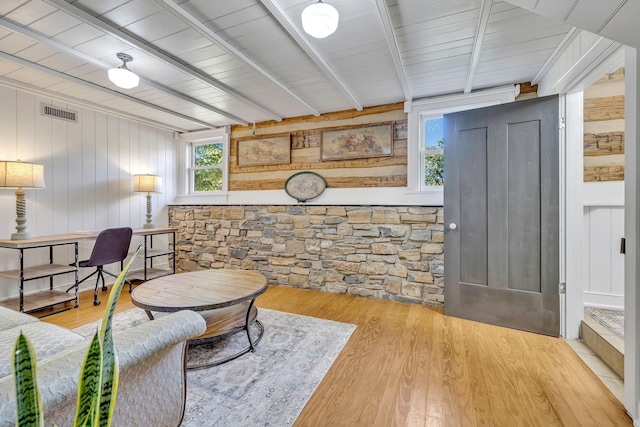 living room featuring beamed ceiling, wooden walls, and light wood-type flooring