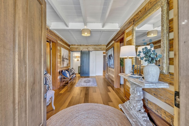 hallway with light hardwood / wood-style floors, a barn door, and beamed ceiling