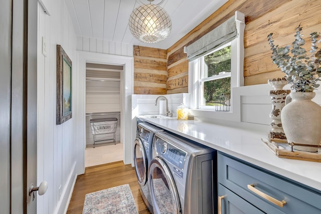 washroom featuring sink, wood walls, cabinets, washer and dryer, and light wood-type flooring