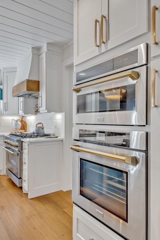 kitchen with premium range hood, tasteful backsplash, white cabinetry, light hardwood / wood-style floors, and stainless steel appliances