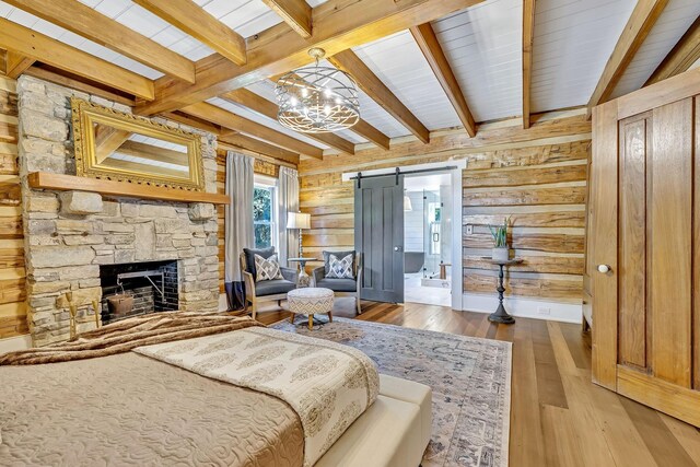 bedroom featuring a fireplace, beamed ceiling, hardwood / wood-style flooring, wooden walls, and a barn door