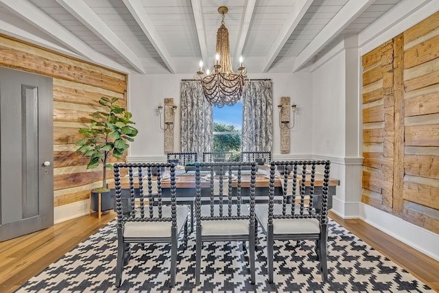 dining room with beamed ceiling, rustic walls, hardwood / wood-style floors, and a notable chandelier