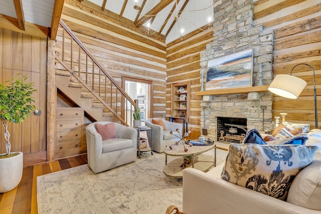 living room featuring hardwood / wood-style floors, a stone fireplace, beam ceiling, high vaulted ceiling, and wooden walls