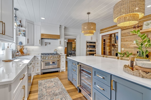 kitchen with light hardwood / wood-style floors, hanging light fixtures, appliances with stainless steel finishes, beverage cooler, and wood ceiling