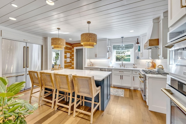 kitchen with custom exhaust hood, a center island, premium appliances, pendant lighting, and white cabinets