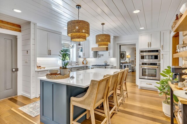 kitchen featuring light hardwood / wood-style floors, a kitchen island, a breakfast bar area, white cabinets, and appliances with stainless steel finishes