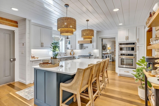 kitchen featuring light hardwood / wood-style flooring, white cabinetry, hanging light fixtures, double oven, and a kitchen island