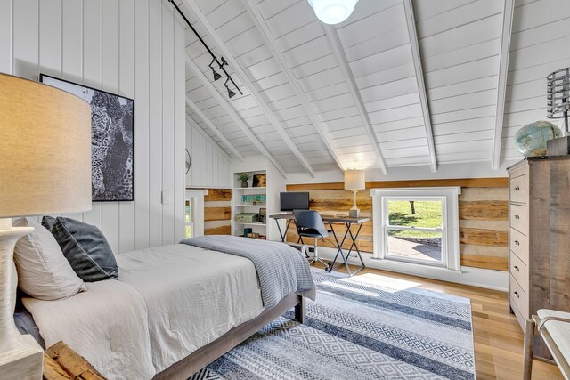 bedroom featuring lofted ceiling with beams, wooden walls, and light wood-type flooring