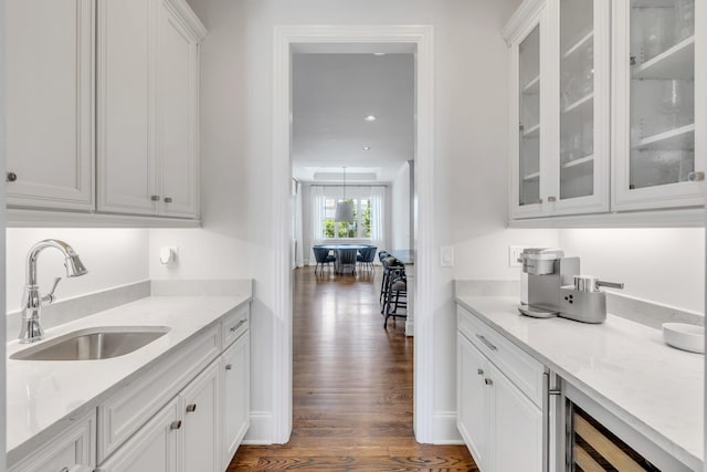 bar featuring light stone counters, beverage cooler, sink, dark hardwood / wood-style floors, and white cabinetry