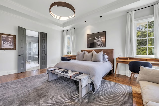 bedroom with hardwood / wood-style flooring, a raised ceiling, ornamental molding, and connected bathroom