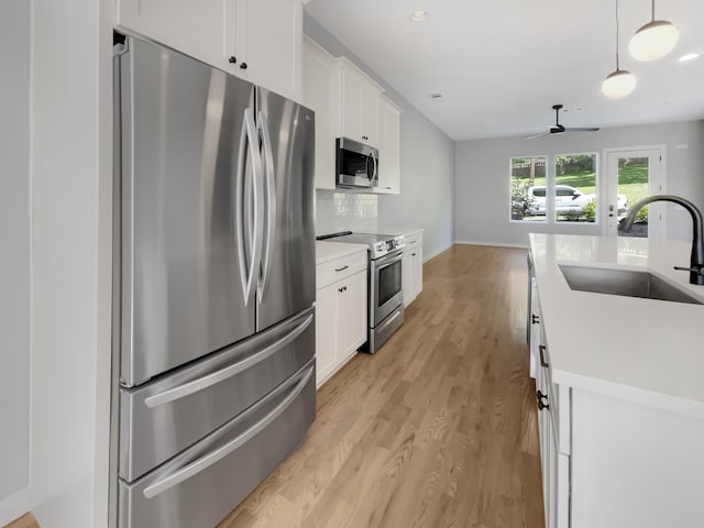 kitchen featuring appliances with stainless steel finishes, white cabinetry, light hardwood / wood-style flooring, and hanging light fixtures