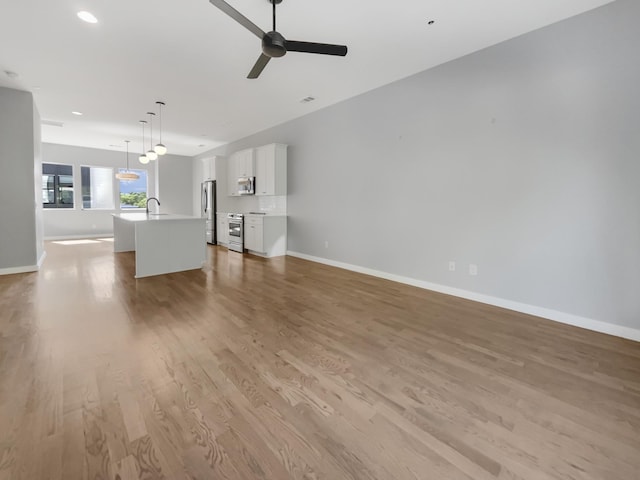 unfurnished living room with light wood-type flooring, ceiling fan, and sink