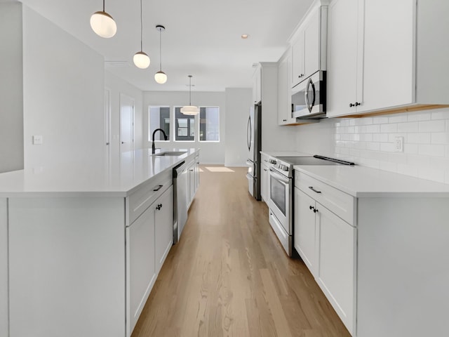 kitchen featuring white cabinets, pendant lighting, an island with sink, and appliances with stainless steel finishes