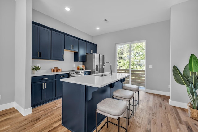 kitchen with blue cabinetry, light hardwood / wood-style flooring, a center island with sink, and a kitchen breakfast bar