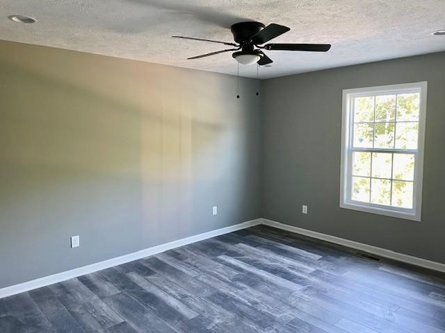 unfurnished room featuring a textured ceiling, a ceiling fan, baseboards, and dark wood finished floors