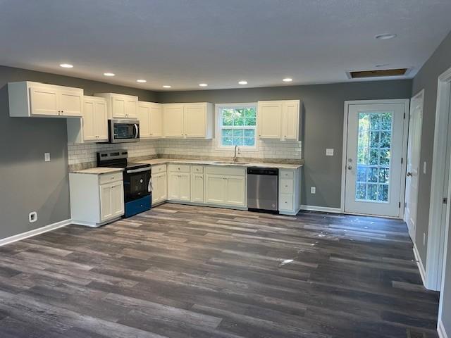 kitchen featuring dark wood-style floors, a sink, stainless steel appliances, baseboards, and white cabinets